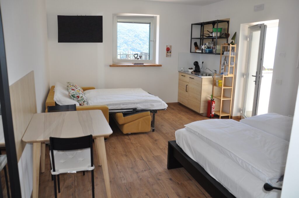Vista completa della camera dell’alloggio Il Fiore del Calisio a Villamontagna, Trento, con letto matrimoniale, divano letto, cucina attrezzata e zona pranzo, ideale per famiglie e piccoli gruppi